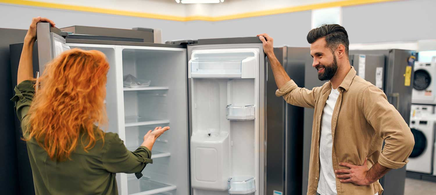 Two people examining an empty refrigerator in a store.